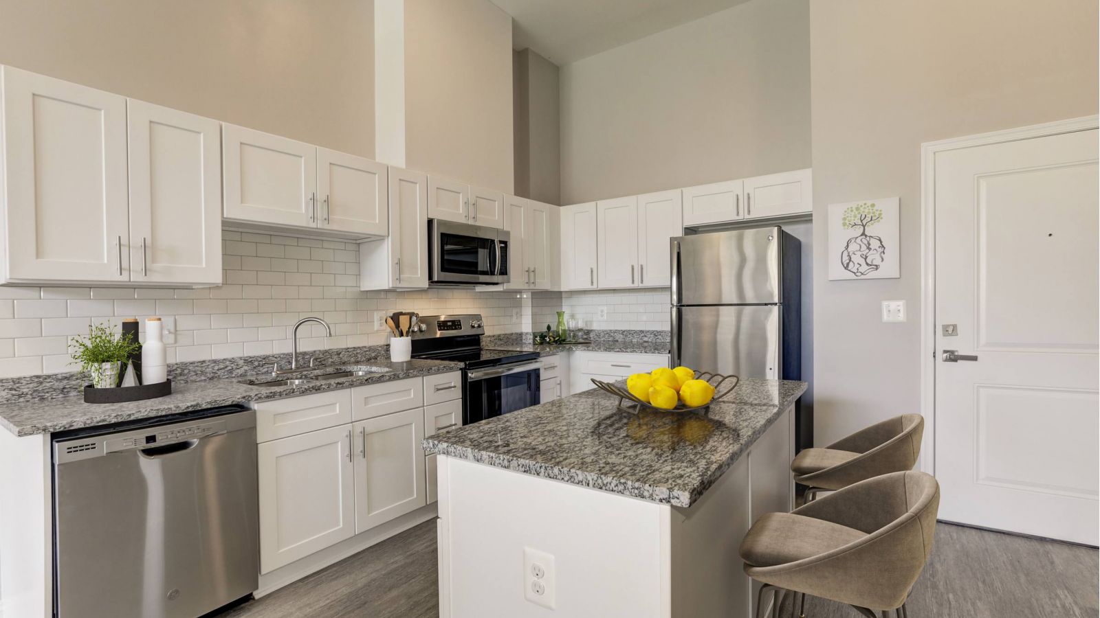Modern kitchen and living area with white cabinets, stainless steel appliances, and a large island. Cozy seating area with a sofa and rug in the background. Bright and inviting atmosphere.
