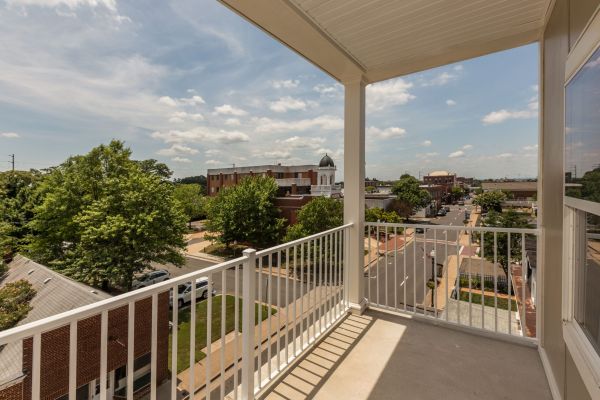 Messenger Place apartment homes with View from a balcony overlooking a small town street, buildings, trees, and a partly cloudy sky.