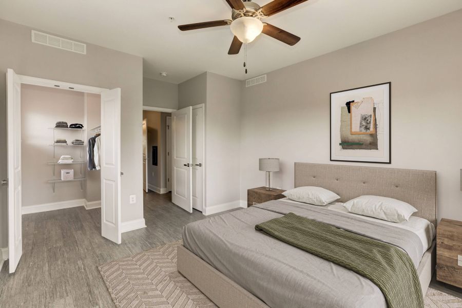 Modern bedroom with beige walls, bed, nightstands, closet, ceiling fan, and framed artwork on the wall.