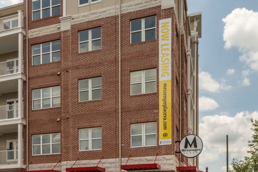 Attain on 5th apartment homes with Red brick apartment building with a large yellow "Now Leasing" banner and a Messenger Place sign.