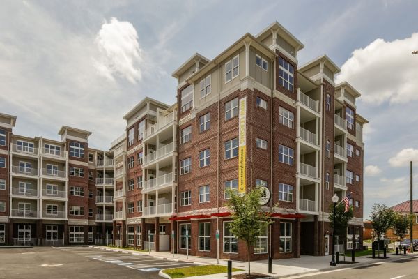 Messenger Place apartment homes with Modern four-story brick apartment building with balconies and large windows, under a partly cloudy sky.