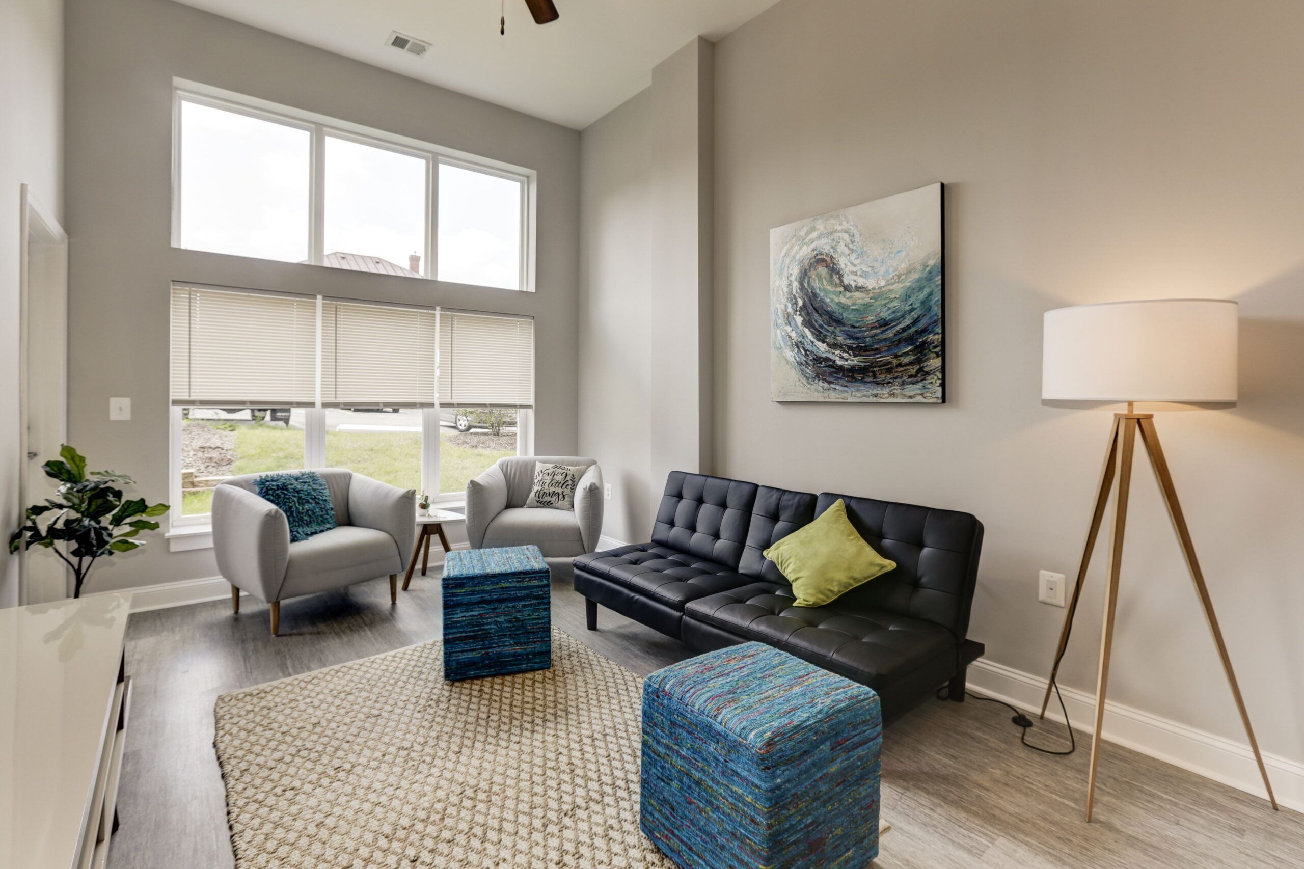 Attain on 5th apartment homes with Modern living room with tall windows, a black sofa, two chairs, blue ottomans, and a floor lamp.