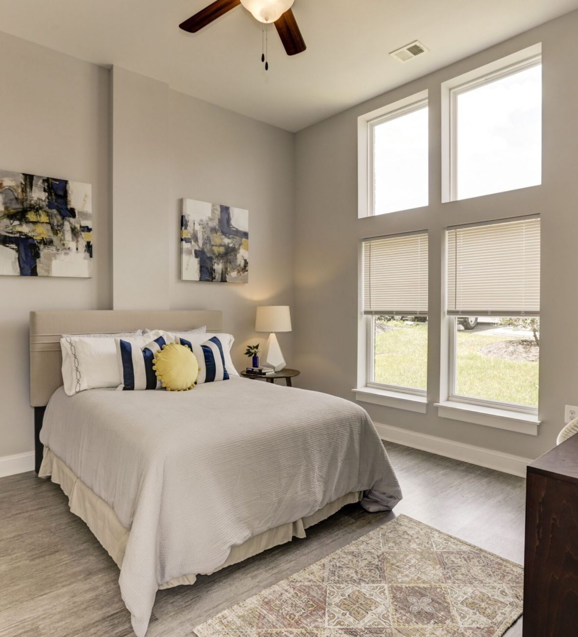 Attain on 5th apartment homes with Bright bedroom with a neatly made bed, modern art, large windows, and a dresser with a decorative vase.