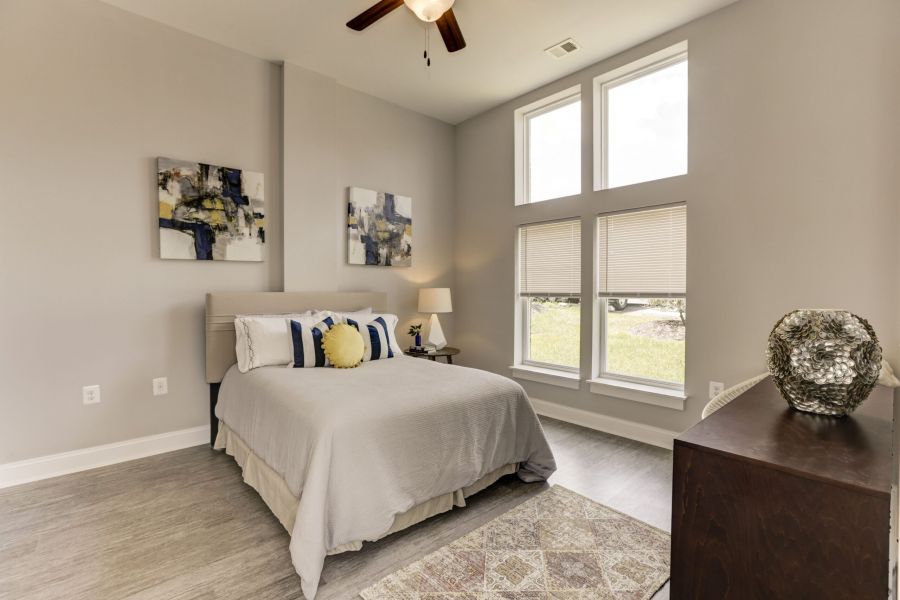 Messenger Place apartment homes with Bright bedroom with a neatly made bed, modern art, large windows, and a dresser with a decorative vase.